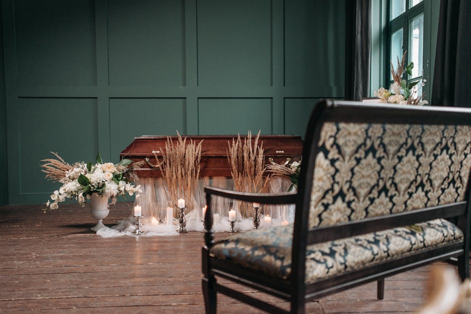A wooden table inside a room with green paneled walls and natural light coming from a large window. The table features floral arrangements including a white ceramic vase filled with white flowers and